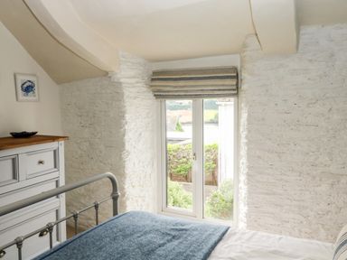 A bedroom with a blue blanket on a bed and white dresser near a window at Alexanders Cottage in Frogmore