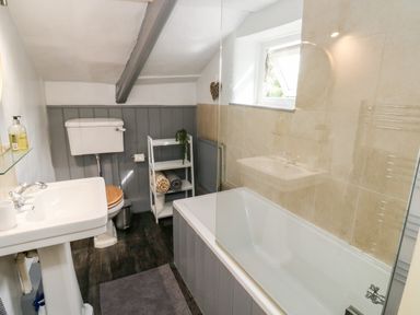 A bathroom with a bathtub a sink a toilet and a small shelving unit at Alexanders Cottage in Frogmore