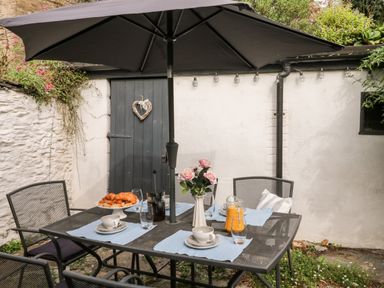 An outdoor patio with a metal table and chairs under a large umbrella at Alexanders Cottage in Frogmore