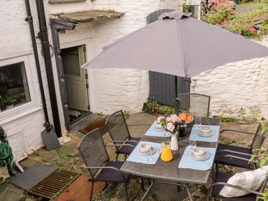 An outdoor patio area with a metal table and chairs under a large umbrella set for breakfast at Alexanders Cottage in Frogmore