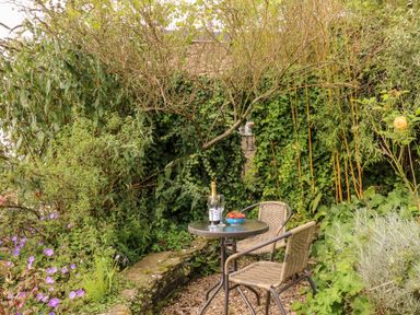 A small garden seating area with a round glass table two chairs a bottle of champagne and a bowl of strawberries at Alexanders Cottage in Frogmore