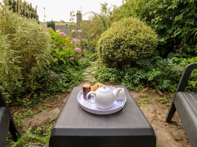 Tea set with a teapot and jar on a tray on a black table in a garden with plants and a stone path at Alexanders Cottage in Frogmore