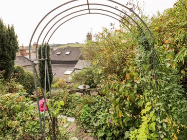 A garden with metal archway and table with chairs surrounded by plants and flowers at Alexanders Cottage in Frogmore