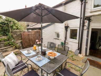 A patio dining table with cups croissants orange juice and an umbrella at Alexanders Cottage in Frogmore