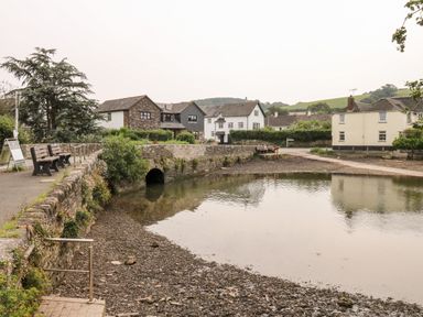 A small water body next to a stone wall with benches and houses in the background at Alexanders Cottage in Frogmore