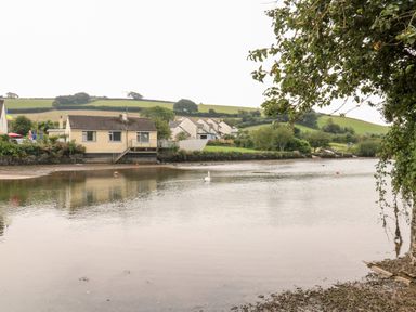 A river with houses on the bank and green hills in the background at Alexanders Cottage in Frogmore