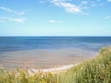 A view of the ocean from a grassy cliff with blue sky and some clouds at Seaward in Trimingham