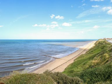 A beach with waves and wooden groynes next to grassy cliffs at Seaward in Trimingham