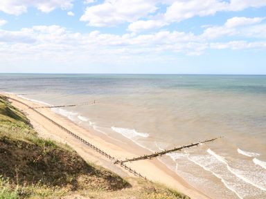A sandy beach with wooden groynes stretching into the sea and grassy cliffs at Seaward in Trimingham
