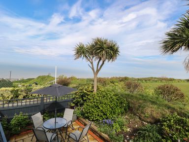 A garden patio with table and chairs and umbrella overlooking greenery and sea at Seaward in Trimingham