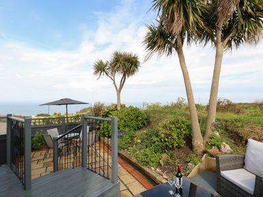 An outdoor patio with a table and chairs under an umbrella and seating area with a bottle and glasses near plants and trees at Seaward in Trimingham