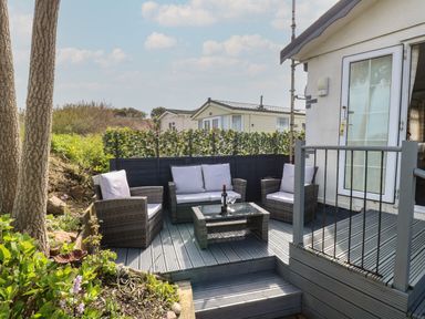 An outdoor seating area with a sofa set and coffee table on a wooden deck next to a white building at Seaward in Trimingham