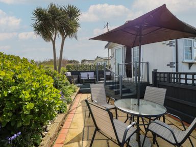 An outdoor patio with a round glass table and four chairs under a large umbrella next to a house with a deck and seating area at Seaward in Trimingham