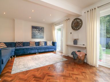 A living room with a blue sectional sofa and pillows a wall clock on the wall and a basket with blankets near glass doors at 4 Woodland Park in Northam