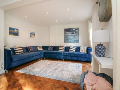 A living room with a blue sectional sofa pillows paintings a table lamp and a rug at 4 Woodland Park in Northam