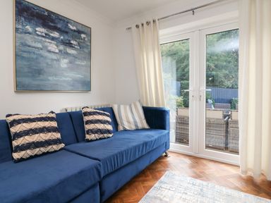 A living room with a blue sofa with cushions and glass doors opening to a garden at 4 Woodland Park in Northam
