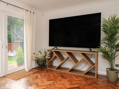 A television on a wooden stand with plants near a glass door in a room at 4 Woodland Park in Northam