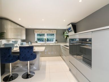 A kitchen with grey cabinets blue bar stools and small kitchen appliances at 4 Woodland Park in Northam