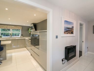 A kitchen with grey cabinets and white countertops next to a hallway with a framed picture and a wall-mounted heater at 4 Woodland Park in Northam