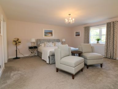 A bedroom with a bed nightstands armchairs a round table window with curtains and a standing fan at 4 Woodland Park in Northam