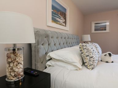 A bedroom with a grey tufted headboard white bedding patterned pillows seashell lamp and framed pictures on walls at 4 Woodland Park in Northam