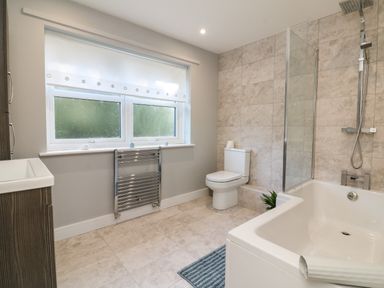 A bathroom with a bathtub shower combination toilet sink window and towel radiator at 4 Woodland Park in Northam
