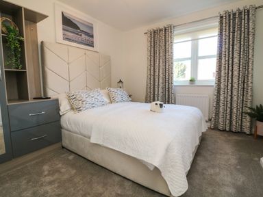A bedroom with a bed white bedspread patterned pillows a window with curtains and a bedside table at 4 Woodland Park in Northam