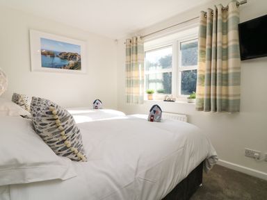 A bedroom with two single beds next to a window with striped curtains and a wall-mounted television at 4 Woodland Park in Northam
