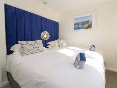 A bedroom with two beds having white bedding blue headboard and coastal decorations at 4 Woodland Park in Northam