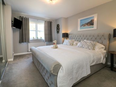 A bedroom with a large bed bedside tables lamps a window with curtains and a wall-mounted television at 4 Woodland Park in Northam