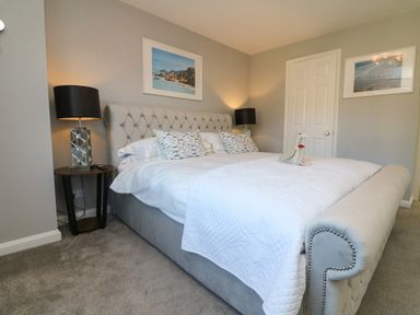 A bedroom with a large upholstered bed with white bedding and patterned pillows at 4 Woodland Park in Northam