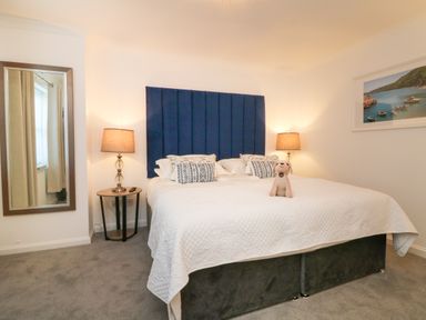 A bedroom with a bed with blue headboard bedside tables with lamps a mirror and a wall picture at 4 Woodland Park in Northam