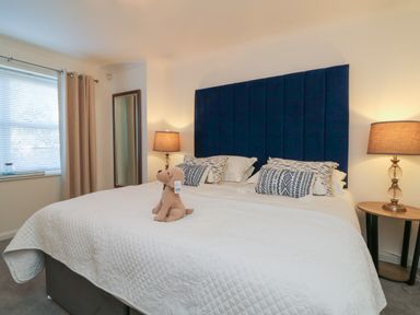 A bedroom with a large bed with a blue headboard and lamps on wooden bedside tables at 4 Woodland Park in Northam