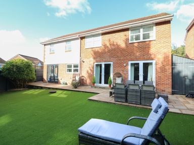 A backyard with artificial grass a patio dining set two hanging chairs and a lounge chair at 4 Woodland Park in Northam