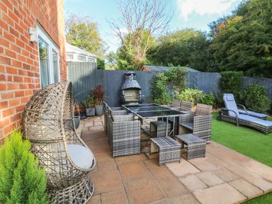 An outdoor patio with wicker chairs and a glass table a barbecue grill and lounge chairs at 4 Woodland Park in Northam