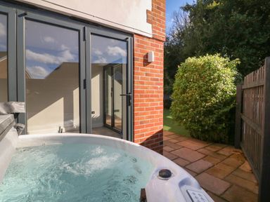 An outdoor patio area with a hot tub next to glass doors and a garden with a bush at 4 Woodland Park in Northam