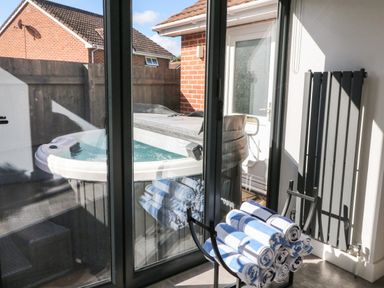 A glass door looking out to a hot tub in a fenced yard with rolled towels on a black metal rack inside the room at 4 Woodland Park in Northam