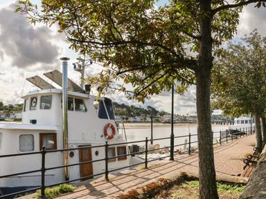 A boat docked along a riverside walkway with trees benches and railings at 4 Woodland Park in Northam
