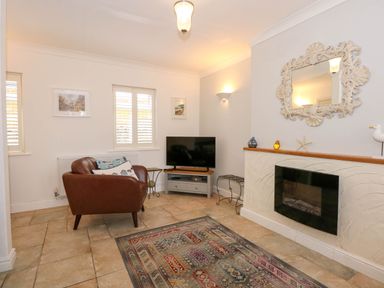 A living room with a leather armchair a television on a stand and a fireplace with a decorative mirror above at Angorfa Bach in Abersoch