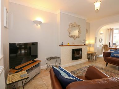 A living room with a television on a stand a fireplace with a decorative mirror and two brown leather chairs at Angorfa Bach in Abersoch