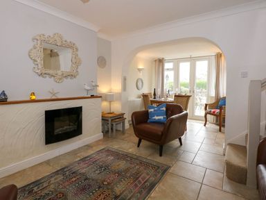 A living room with a brown chair, a fireplace, and a dining area with a table and chairs in the background at Angorfa Bach in Abersoch