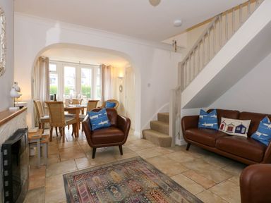 A living room with brown leather chairs and sofa a patterned rug and a dining table with wicker chairs at Angorfa Bach in Abersoch