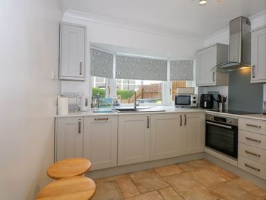 A kitchen with light gray cabinets stools and appliances at Angorfa Bach in Abersoch