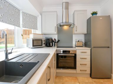 A kitchen with a sink a microwave an air fryer an oven a stovetop a toaster a refrigerator and cabinets at Angorfa Bach in Abersoch