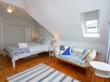 A bedroom with a bed side table a small sofa and skylight window at Angorfa Bach in Abersoch