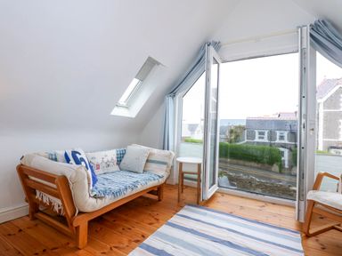 A sitting area with a sofa chair a small round table and an armchair near a large open window at Angorfa Bach in Abersoch