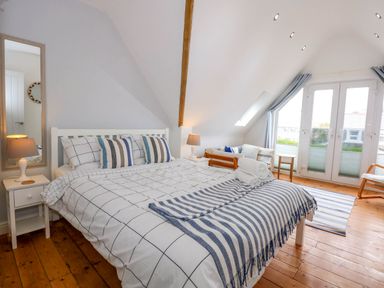 A bedroom with a large bed pillows and bedside tables with lamps next to a small sofa and large windows at Angorfa Bach in Abersoch