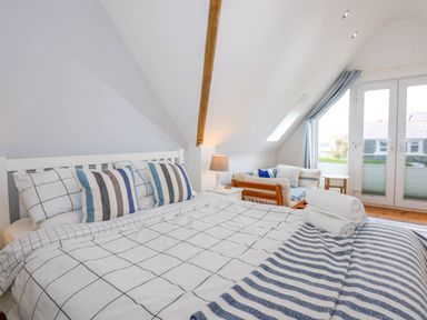 A bedroom with a bed with striped and checkered bedding a wooden framed couch a small table and glass doors at Angorfa Bach in Abersoch