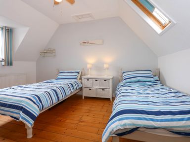 A bedroom with two single beds with striped bedding and a small white cabinet with lamps at Angorfa Bach in Abersoch