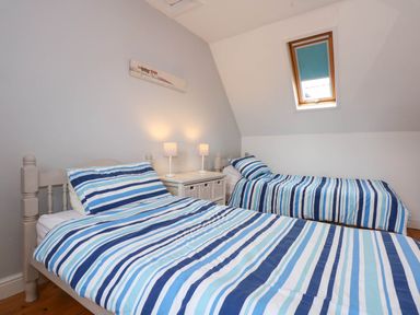 A bedroom with two single beds with striped bedding and a bedside table with two lamps at Angorfa Bach in Abersoch